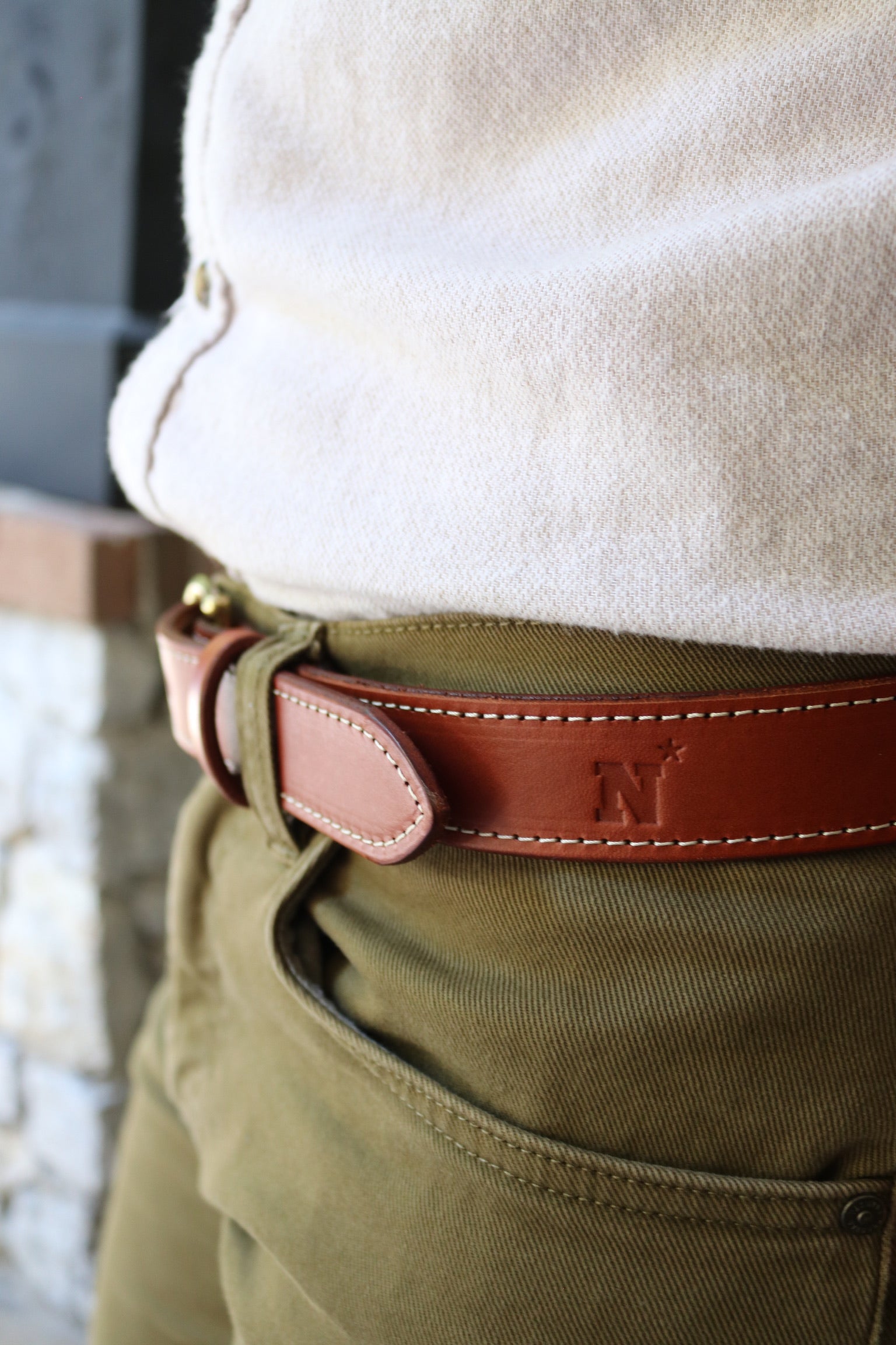 Brown leather belt with a Naval Academy N-star logo on green pants against a blurred background
