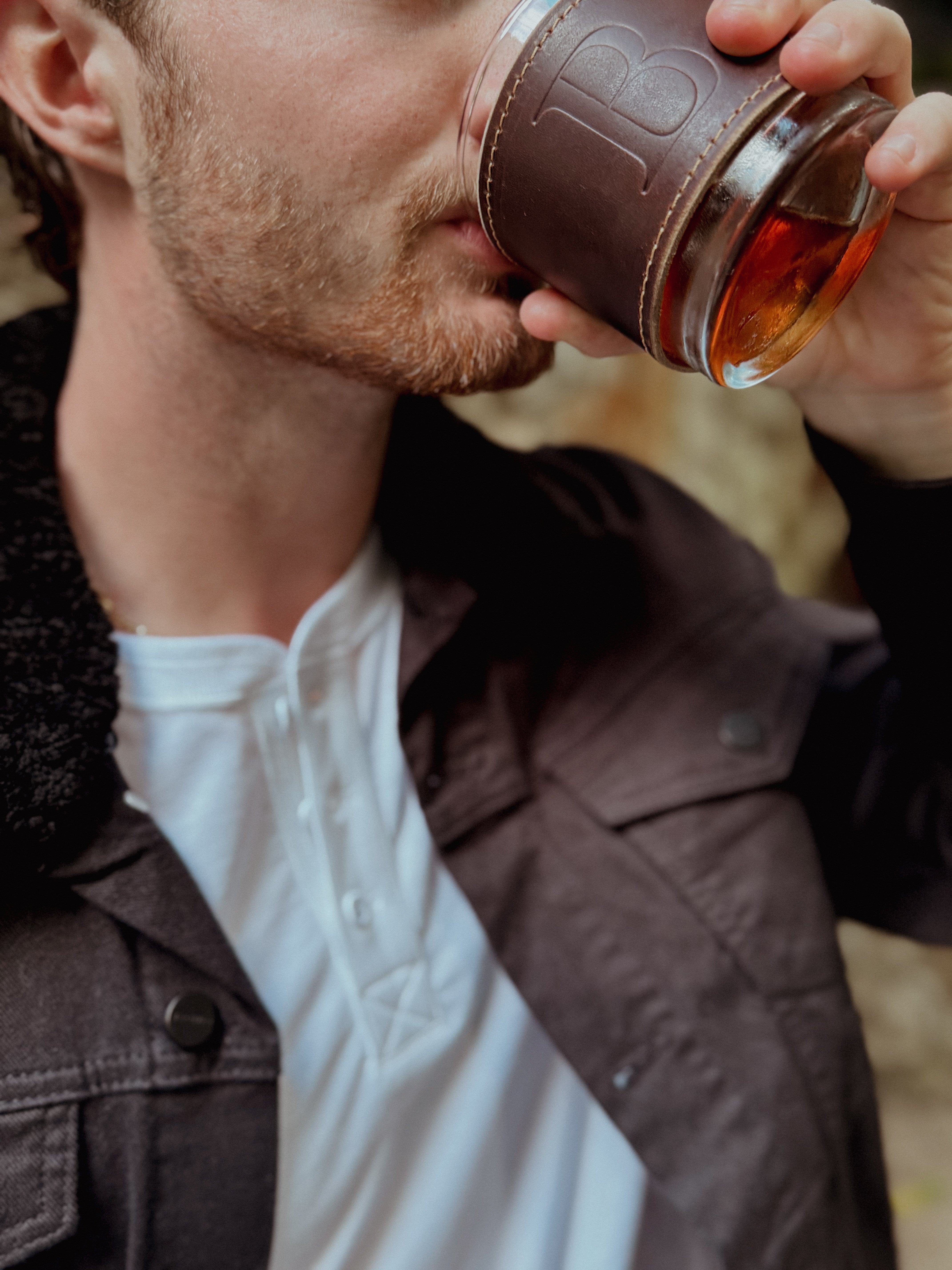 Man drinking from a leather wrapped whiskey glass featuring a debossed monogram